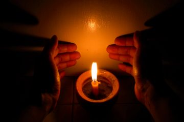 Hands cupping around a burning candle